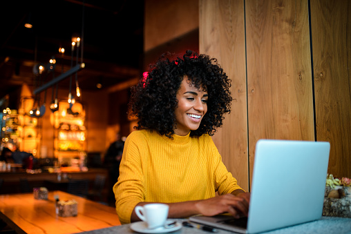 Beautiful smiling African American woman using laptop at the bar.